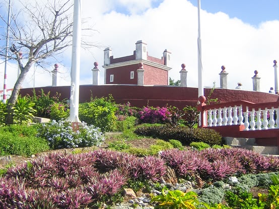 Historic building in Holguín, Cuba, surrounded by flowering gardens.