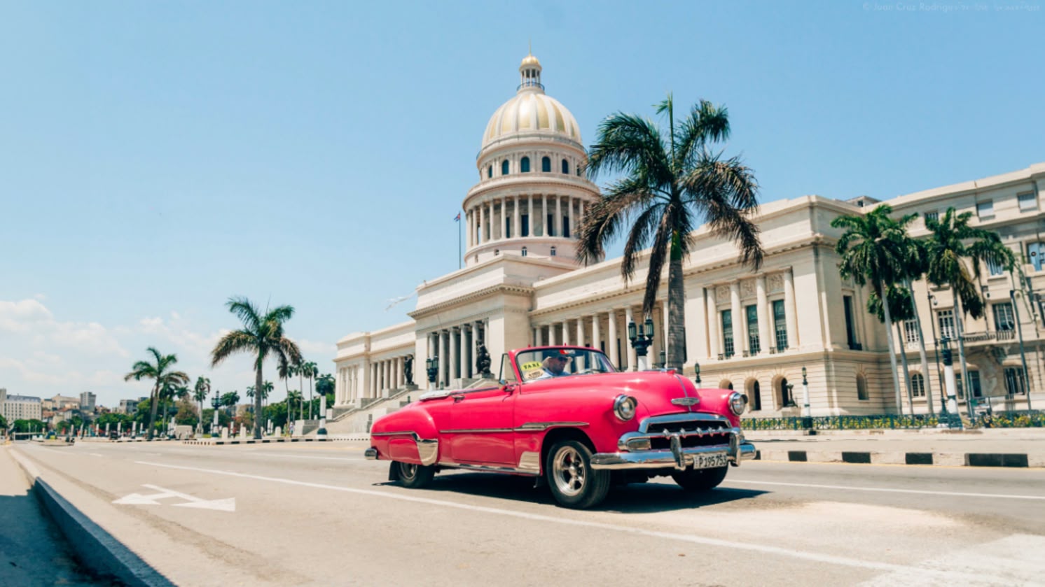 Klasyczny samochód przejeżdża przed budynkiem Kapitolu w Hawanie, Kuba, łącząc historyczny urok z tropikalnym klimatem miasta.